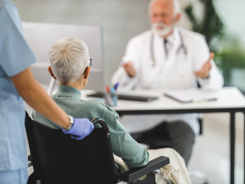Paciente em cadeira de rodas acompanhada em consulta médica